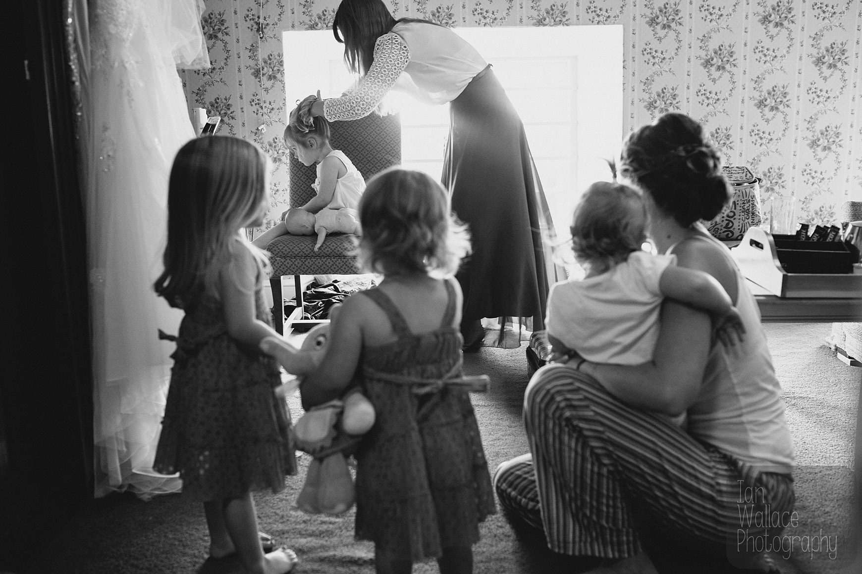 Flower-girls and bride look on as the hairdresser works her magic during bridal preparation