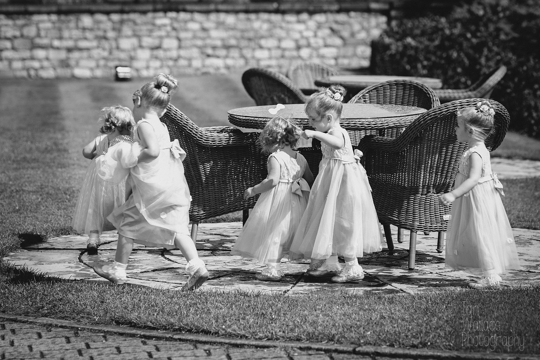 Flower-girls running around a table outside as the sun breaks through the rain.