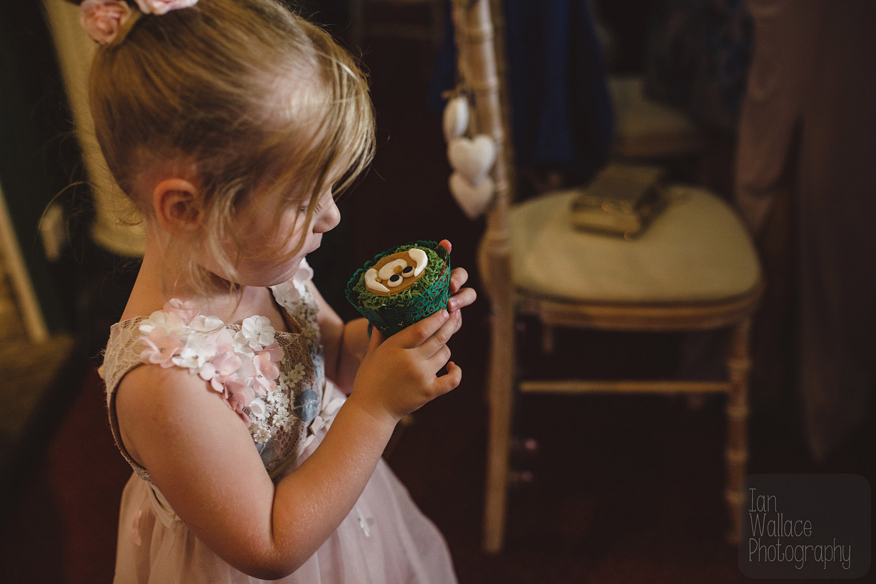 Flower-girl studying her cup cake which is about to be devoured.