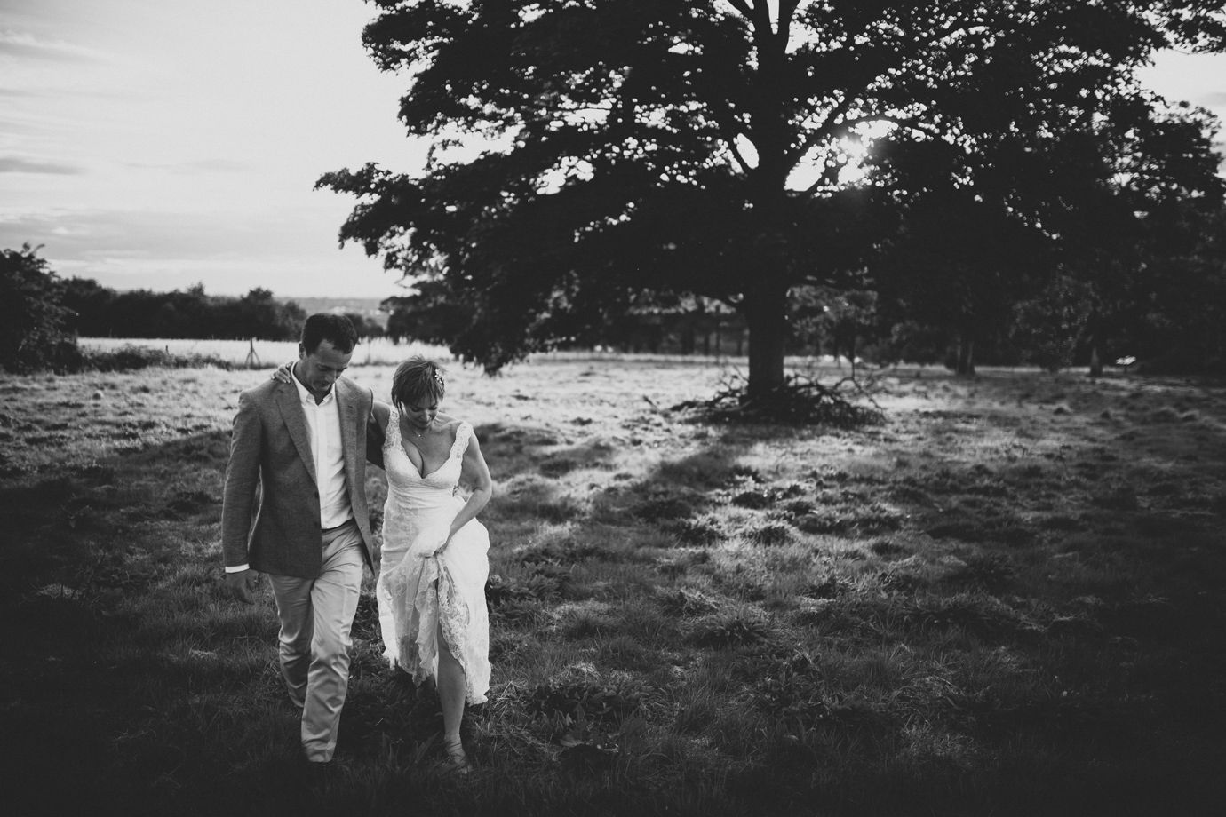 Couple strolling across a field against a sunset, documentary wedding photography