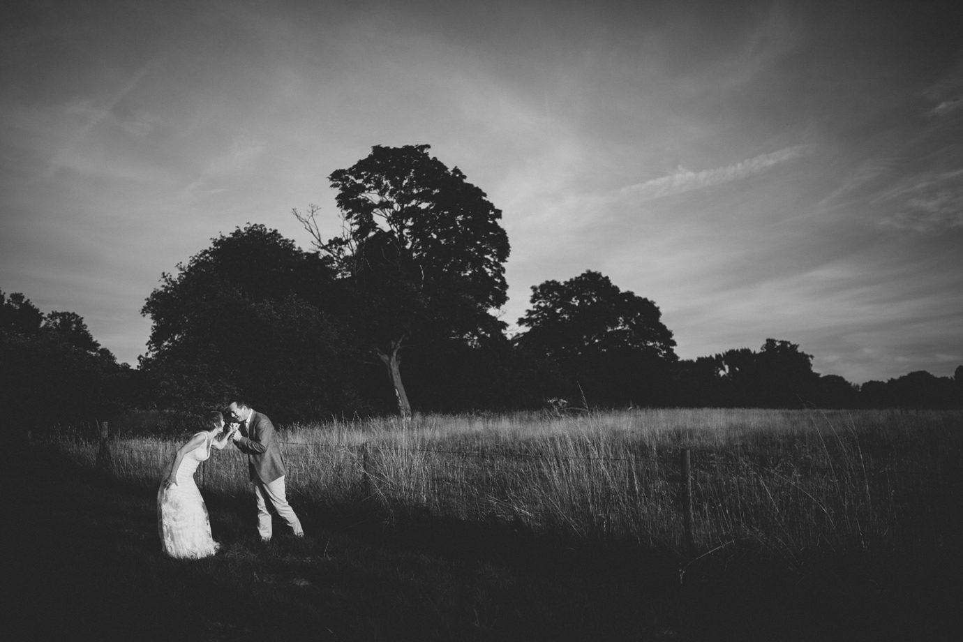 Bride and groom playing in field during sunset, modern wedding photography